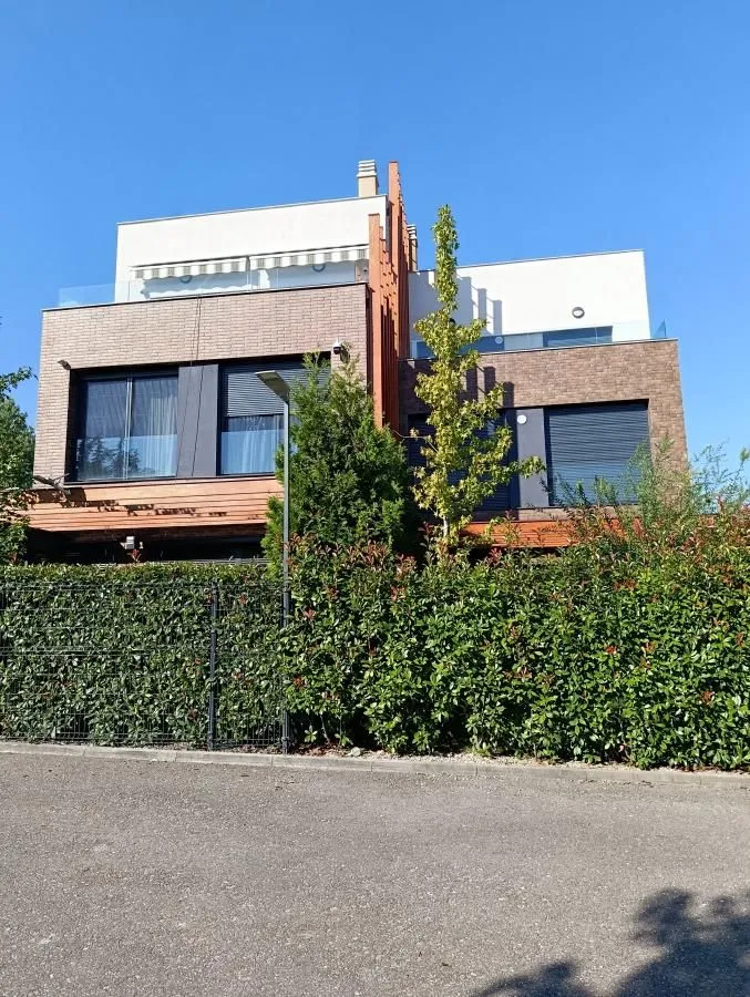 View of the exterior of a modern residential building with a landscaped yard and greenery.