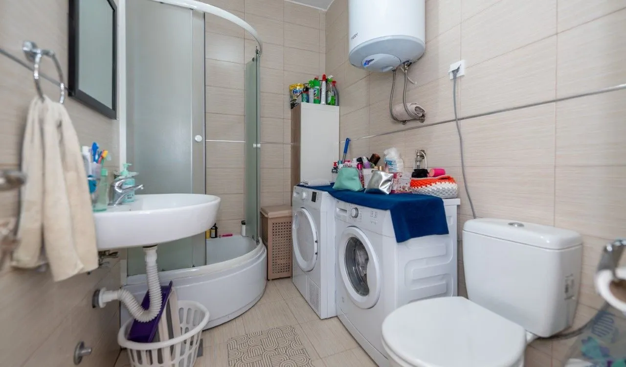 Bathroom with a shower cabin, washbasin, washing machine, and toilet.