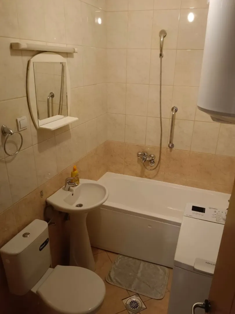 Smaller bathroom with a bathtub, washbasin, toilet, and washing machine.