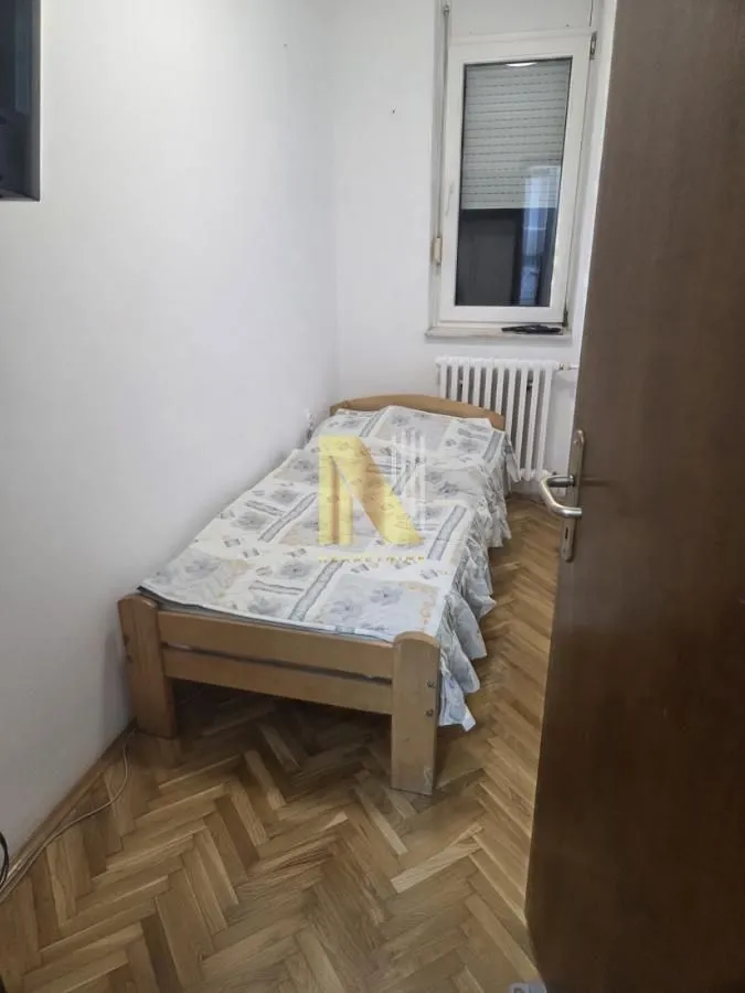 Manja spavaća soba sa drvenim krevetom i parketom na podu.