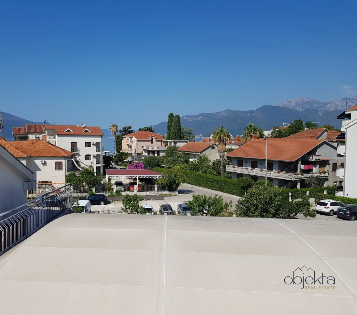 Pogled sa terase na naselje, okolne kuće i planine u daljini.