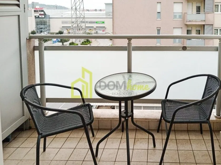 Namješten balkon sa stolom i dvije stolice i pogledom na grad.