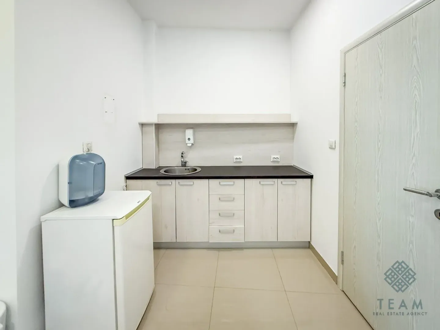 Small kitchenette with white units, a sink, and a small refrigerator.
