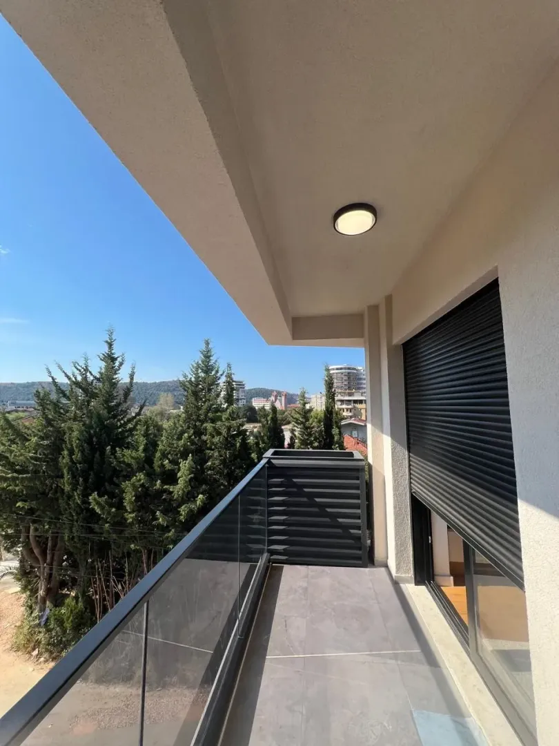 Covered balcony with a glass railing and a view of greenery and surrounding buildings.