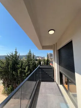 Covered balcony with a glass railing and a view of greenery and surrounding buildings. - image 5