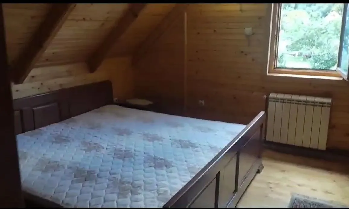 Spavaća soba u potkrovlju obložena drvetom sa velikim bračnim krevetom.