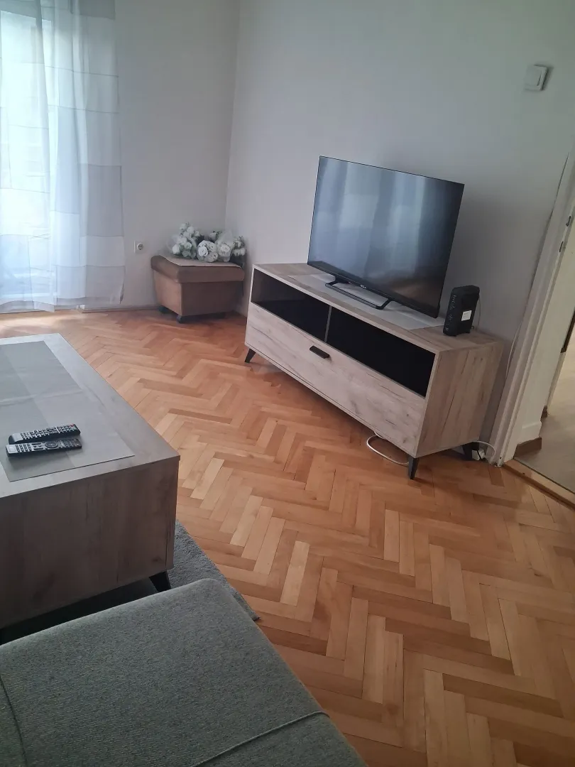 Dnevna soba sa garniturom, TV komodom i parketom na podu.