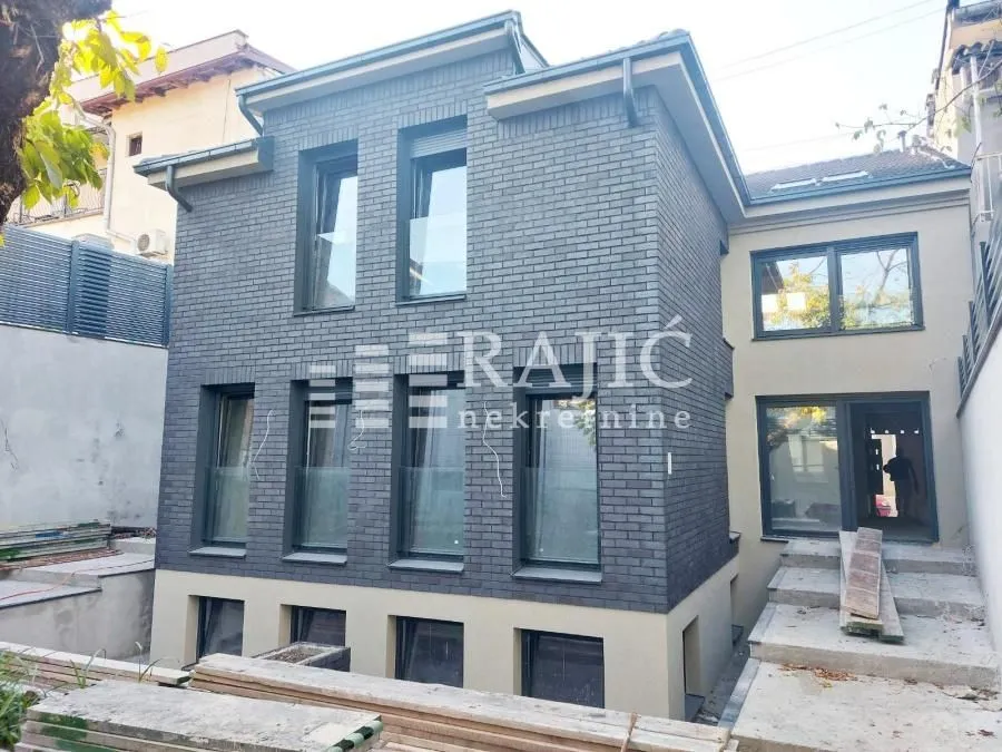 Spoljašnji izgled moderne kuće sa tamnom ciglom i uređenim dvorištem.