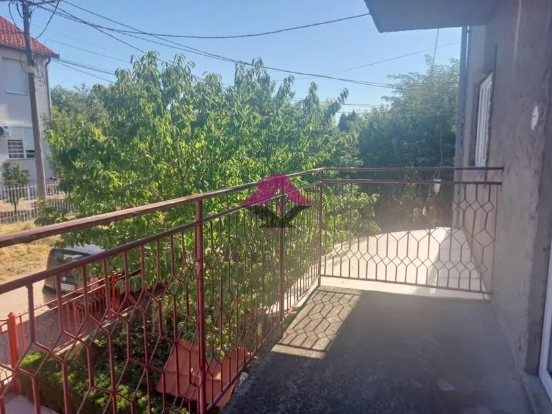 Balkon sa metalnom ogradom i pogledom na zelenilo i ulicu.