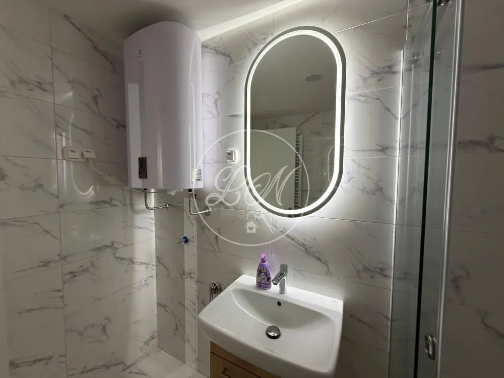 Modern bathroom with a sink, backlit mirror, and water heater.
