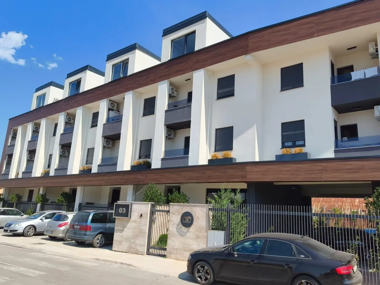 Exterior view of a modern residential building with parking and entrance gate.