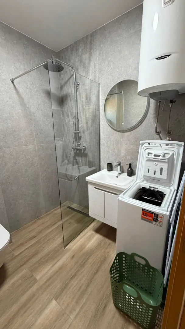 Modern bathroom with a walk-in shower, washbasin, and washing machine.