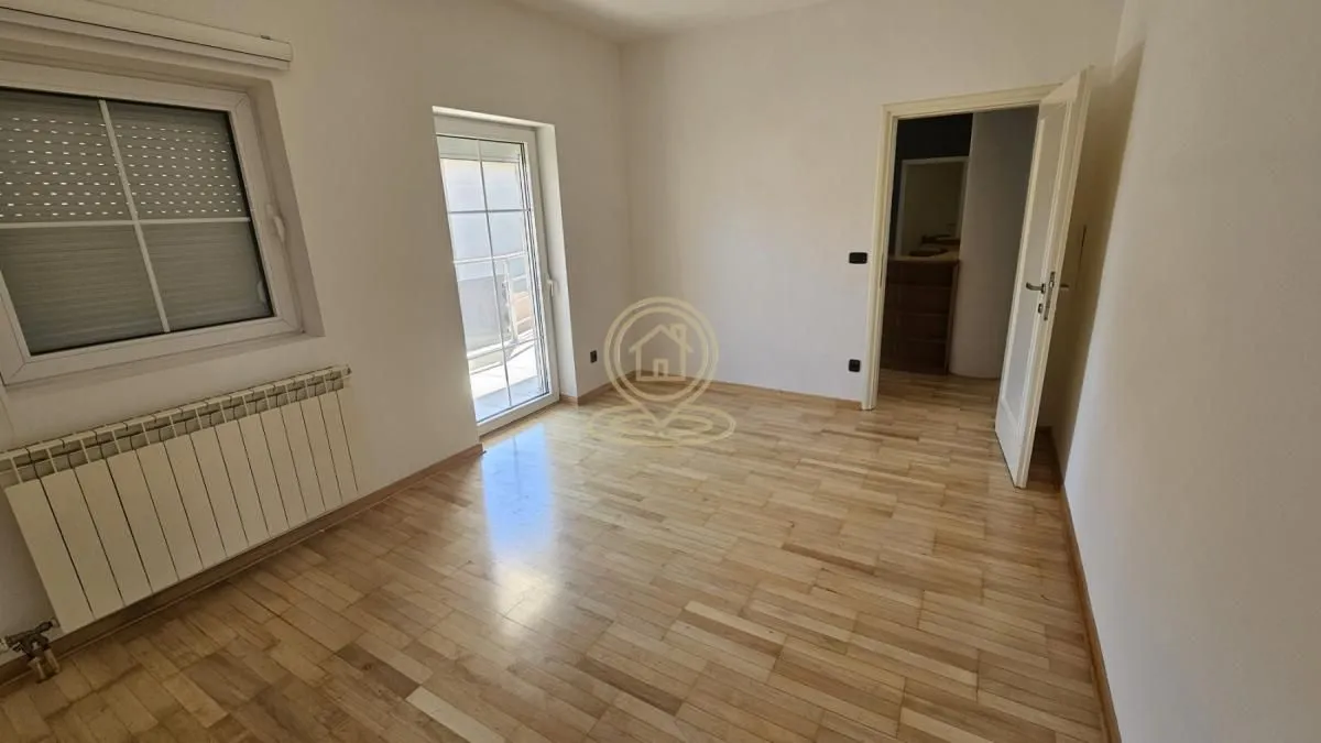 Empty room with wooden flooring, a window, and a door leading to a hallway.