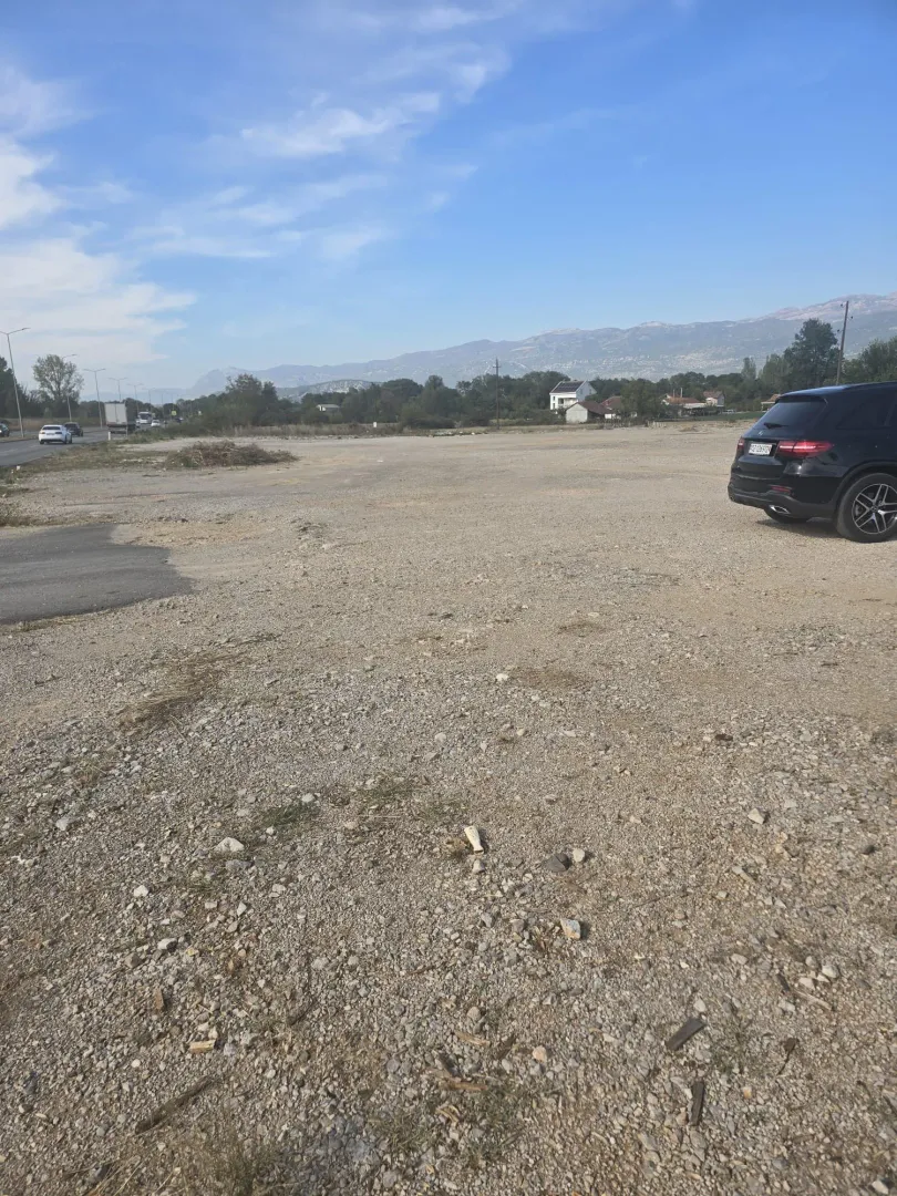 Pogled na prostrani šljunkoviti plac sa parkiranim automobilom.
