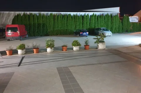 Illuminated paved yard with parking and potted plants at night. - image 19