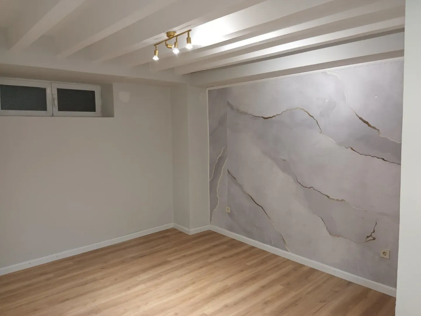 An empty room with a decorative accent wall and laminate flooring.