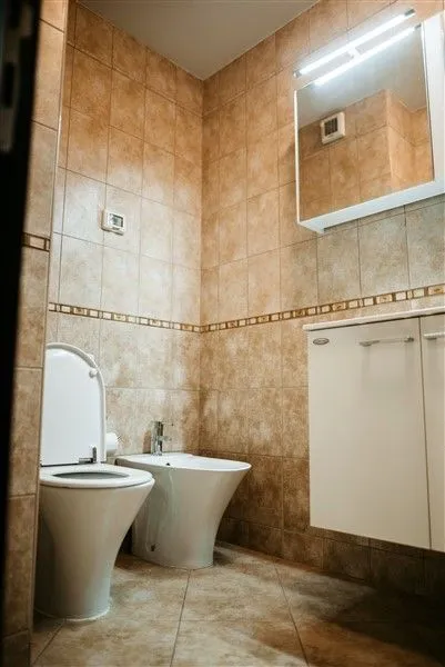 A simple bathroom featuring a toilet, bidet, and beige tiling.