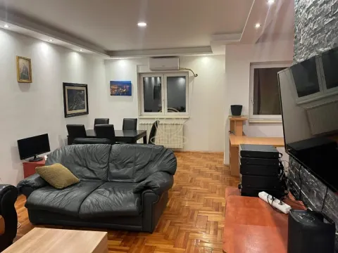 Living room with a sofa, TV, and a dining table in the background. - image 2