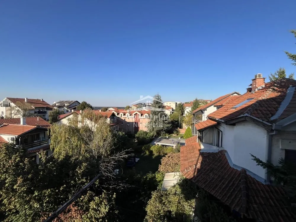 Pogled sa prozora na okolne kuće i krovove sa zelenilom.