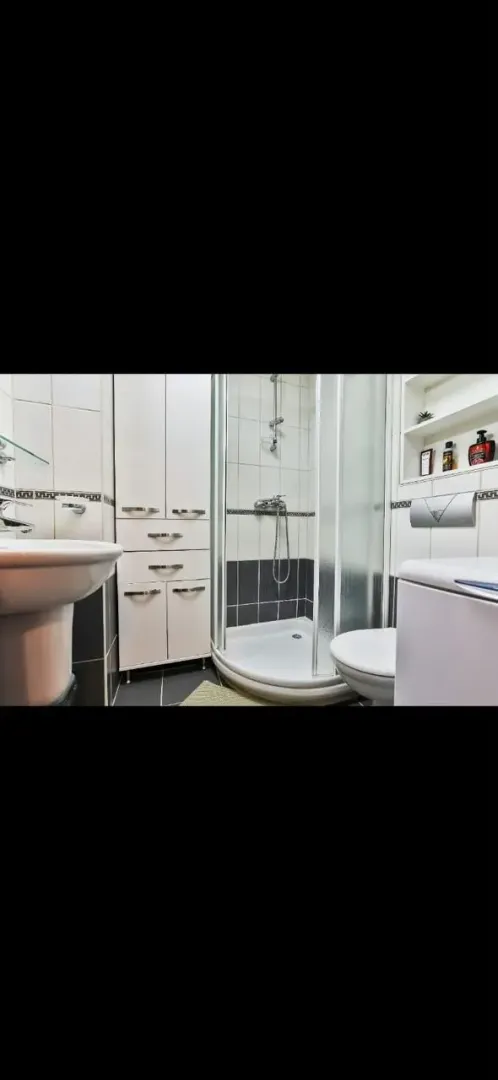 Compactly arranged bathroom with a shower cabin, sink, and white storage units.