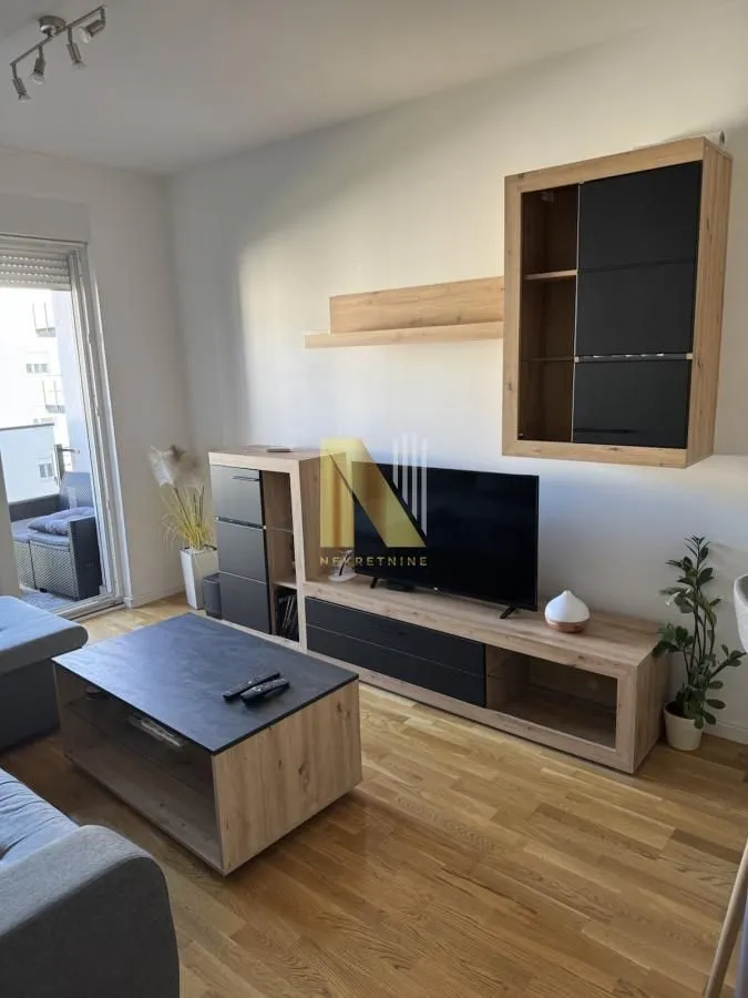 Dnevna soba sa garniturom, TV komodom i izlazom na terasu.