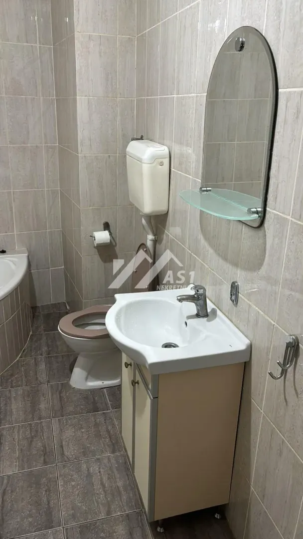 Kupatilo opremljeno umivaonikom, WC šoljom i ogledalom sa policom.