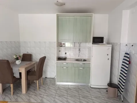 Manja kuhinja sa bijelom i zelenom elementima, frižiderom i trpezarijskim stolom sa stolicama. - image 4