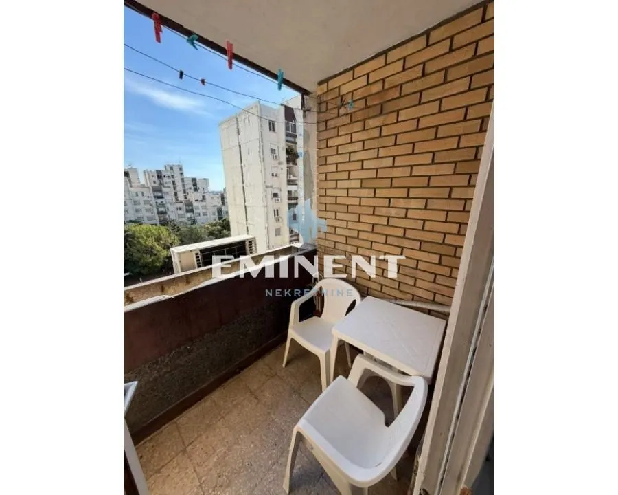 Small furnished balcony with seating furniture and a view of surrounding buildings.