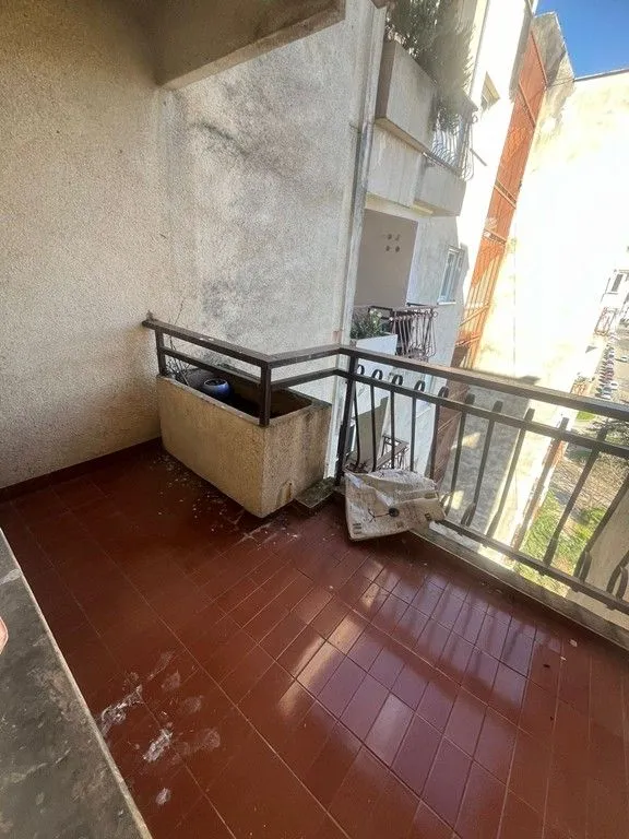 Nenamješten balkon sa popločanim podom i metalnom ogradom.
