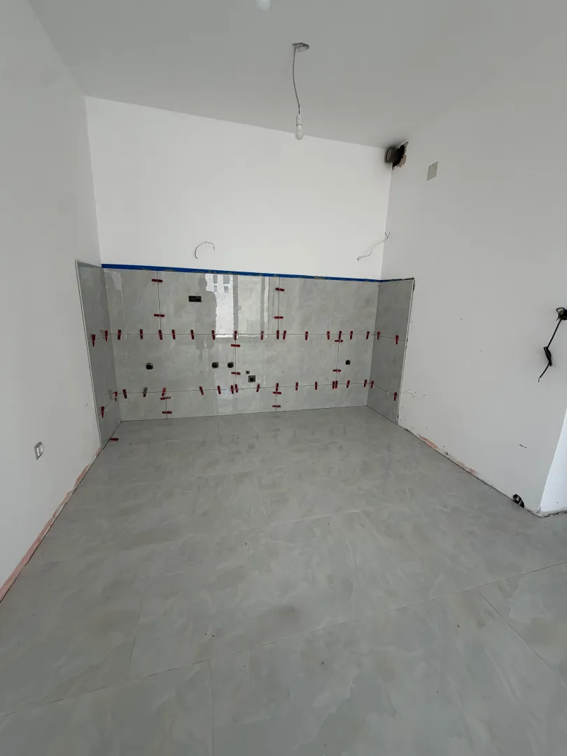 Unfinished kitchen with installed tiles and prepared plumbing and electrical installations.