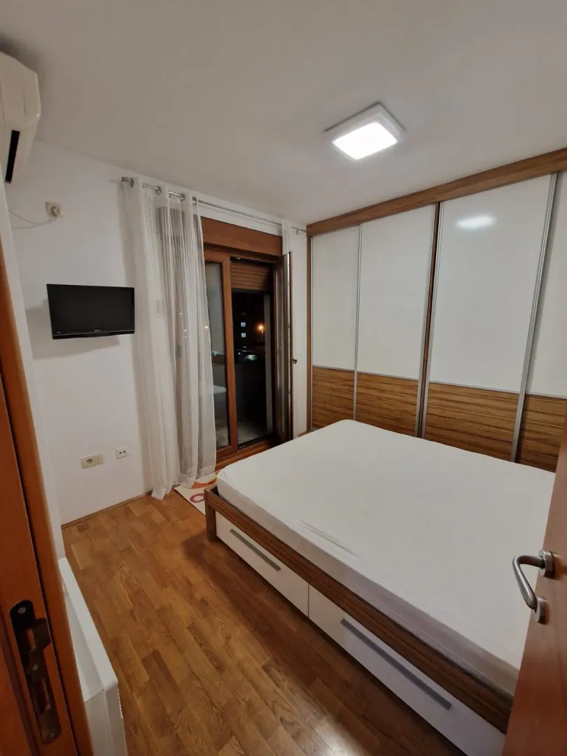 Svijetla spavaća soba sa velikim ugradnim plakarom i izlazom na balkon.