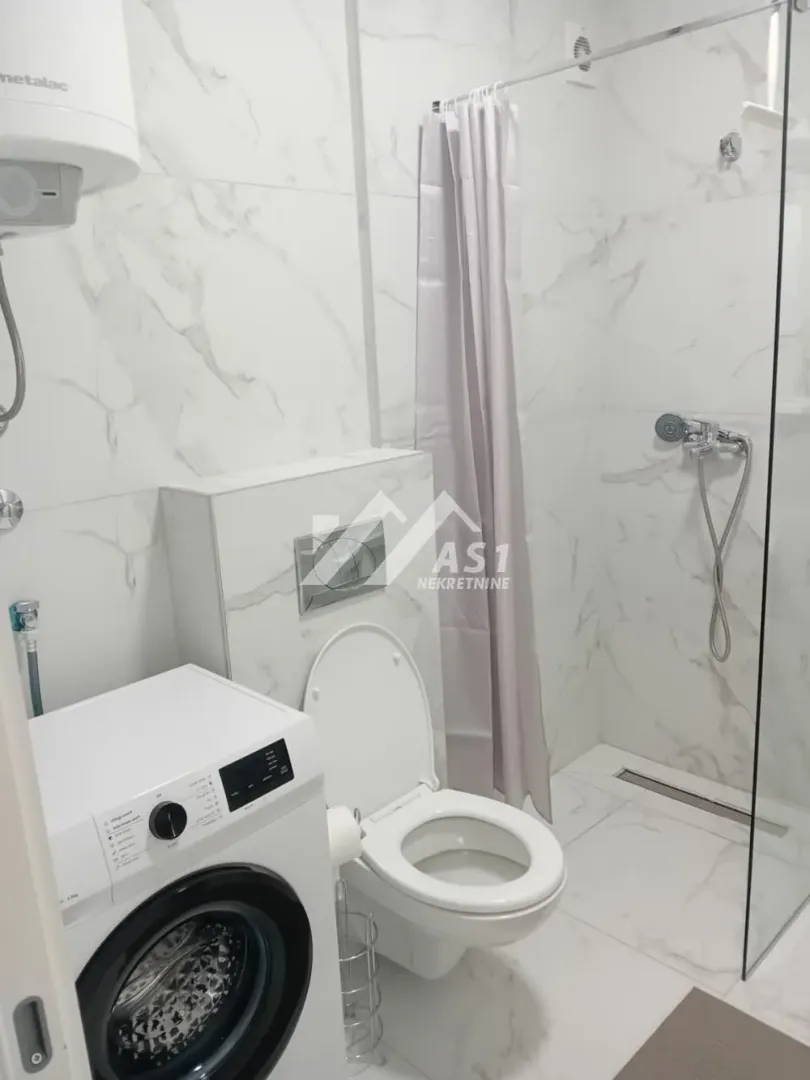 Savremeno opremljeno kupatilo sa tuš kabinom, WC šoljom i veš mašinom.