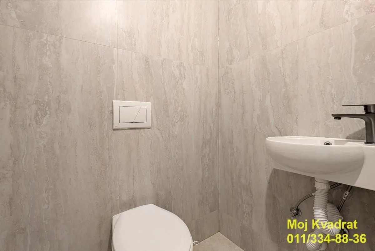 Manje kupatilo obloženo keramičkim pločicama sa umivaonikom i šoljom.