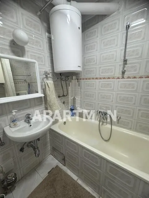 Smaller bathroom with a bathtub, washbasin, and a wall-mounted water heater.