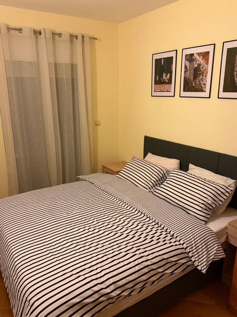 Namještena spavaća soba sa bračnim krevetom, zavjesama i slikama na zidu.