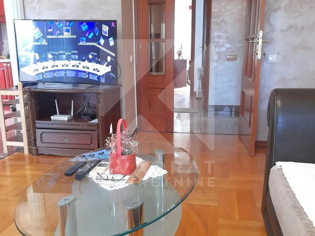 Dnevni boravak sa garniturom, televizorom i drvenim stolom.