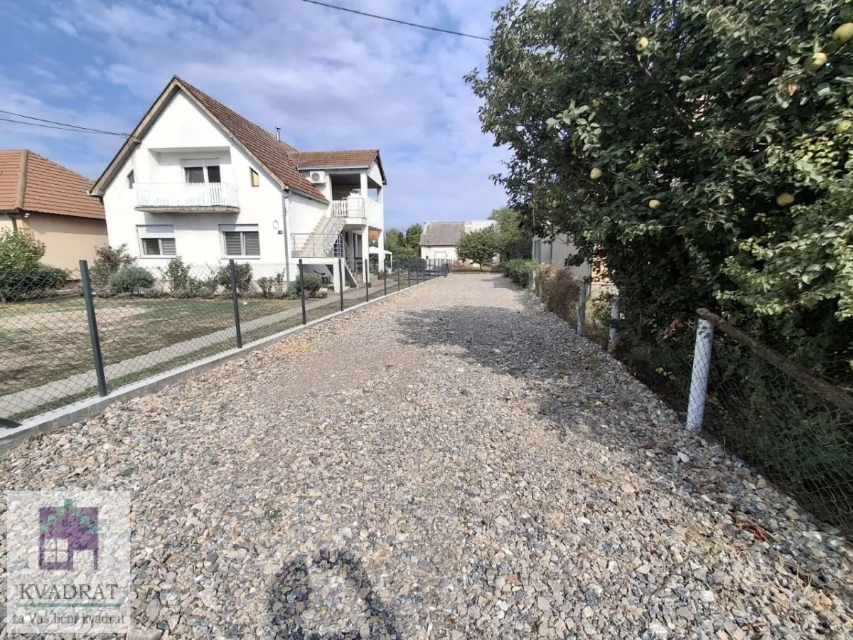 Pogled na dvorište i prilaz kuće sa šljunkom i ogradom.