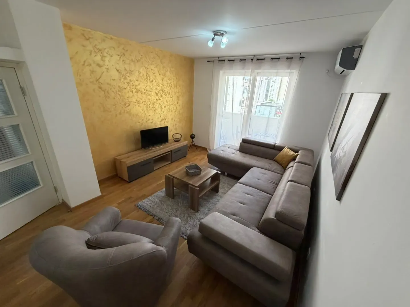 Spacious living room with a sectional sofa, TV unit, and a gold accent wall.