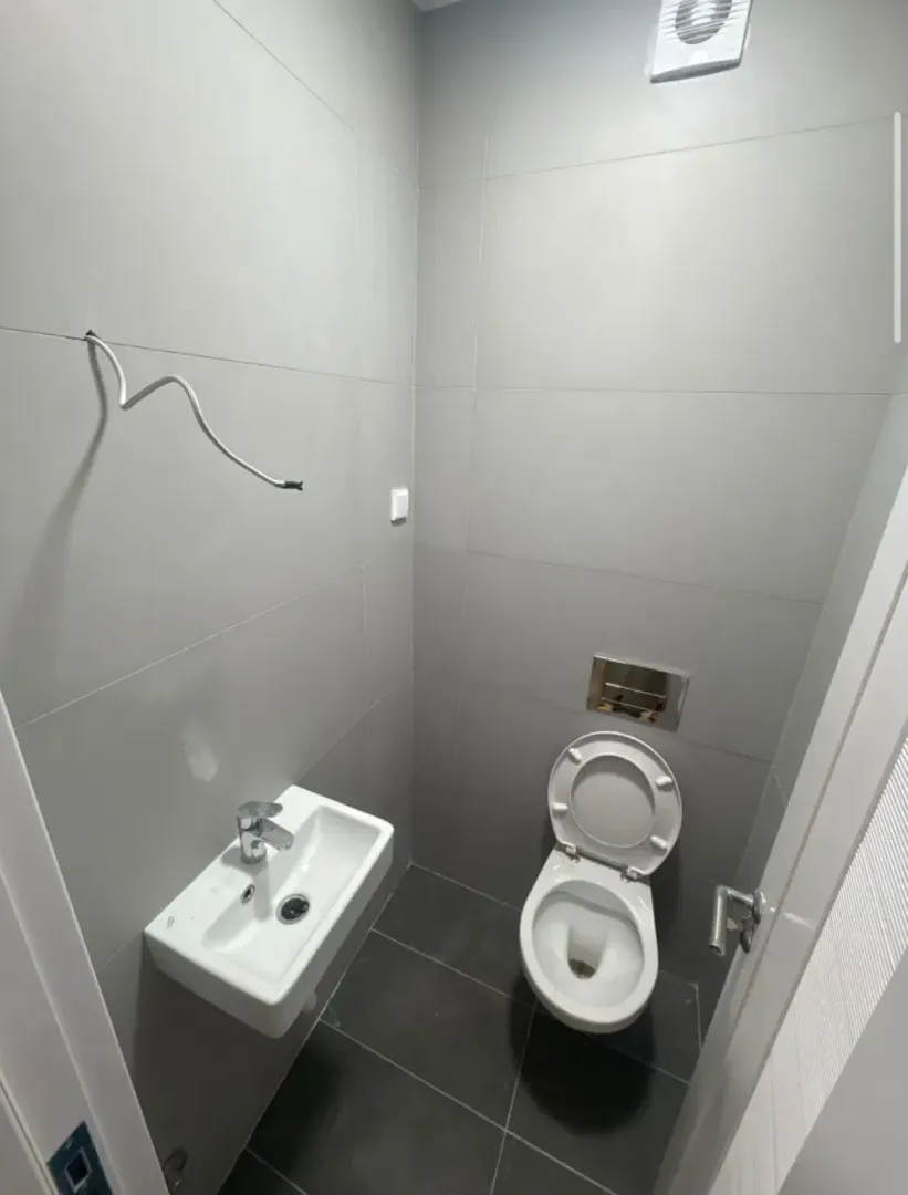 Small bathroom tiled in grey with a toilet and washbasin.