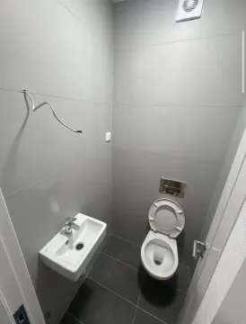 Small bathroom tiled in grey with a toilet and washbasin. - image 3