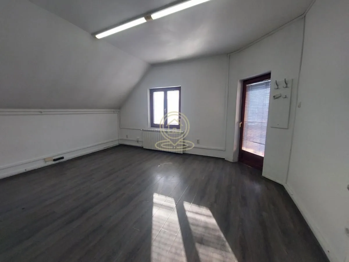 Empty attic room with dark laminate flooring, white walls, and a door leading to a terrace.