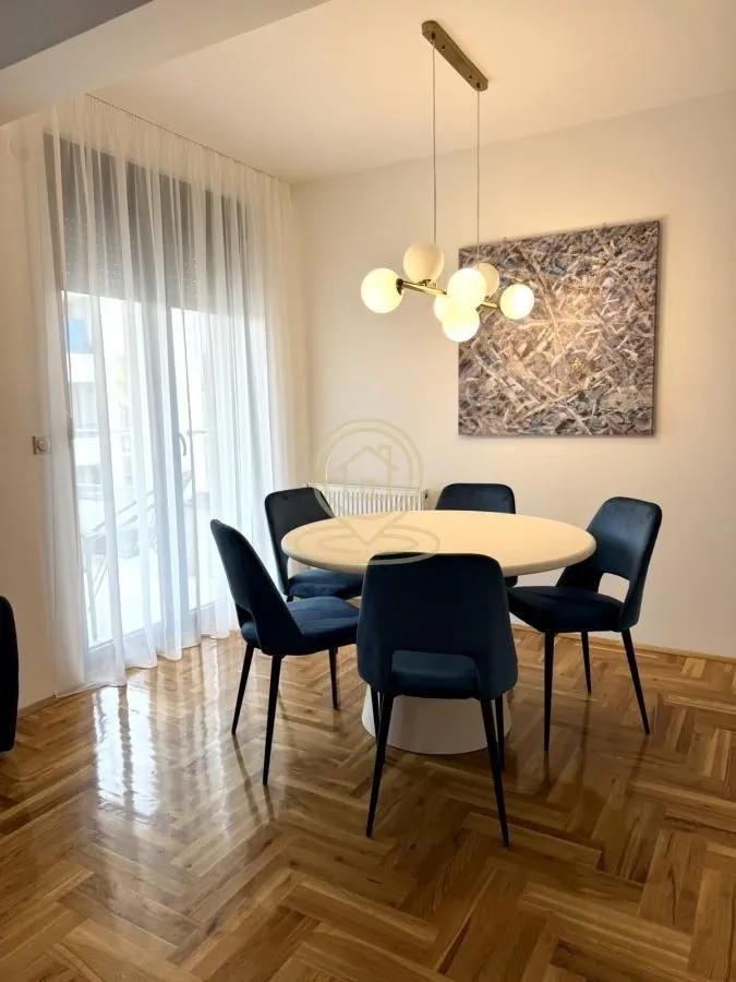 Dining area with a round table, blue chairs, and a chandelier.