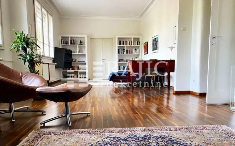 Spacious living room with wooden flooring, bookshelves, and a desk.