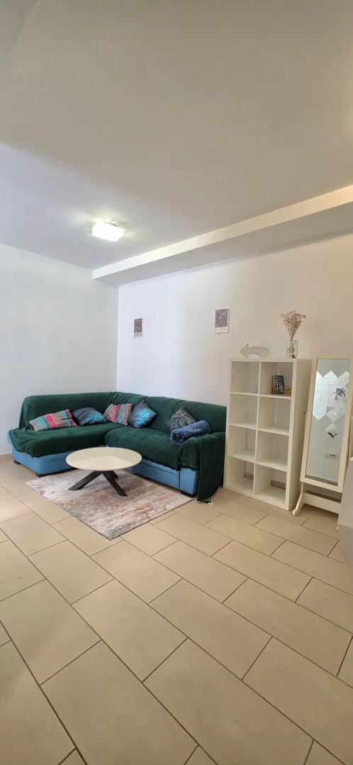 Living room with a green sectional sofa, a white shelving unit, and a coffee table.