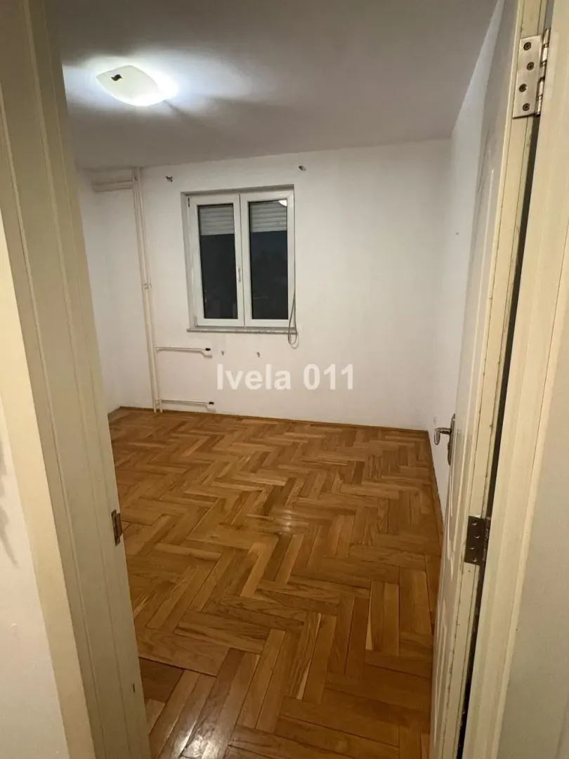 Prazna soba sa parketom i belim zidovima gledana kroz otvorena vrata.