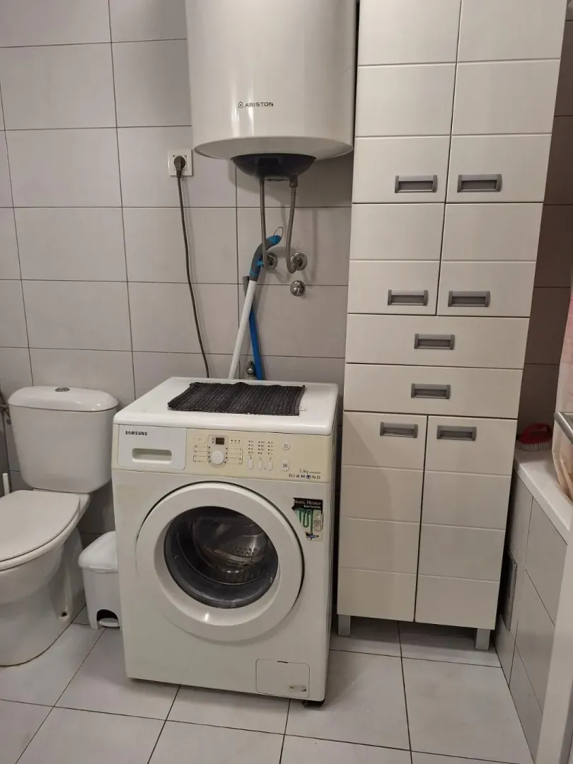 Small bathroom with a washing machine, water heater, and white storage cabinets.