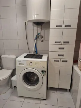 Small bathroom with a washing machine, water heater, and white storage cabinets. - image 8