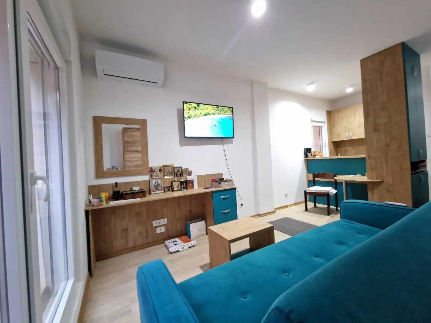Living room with a blue sofa, TV, and desk, looking towards the kitchen area.