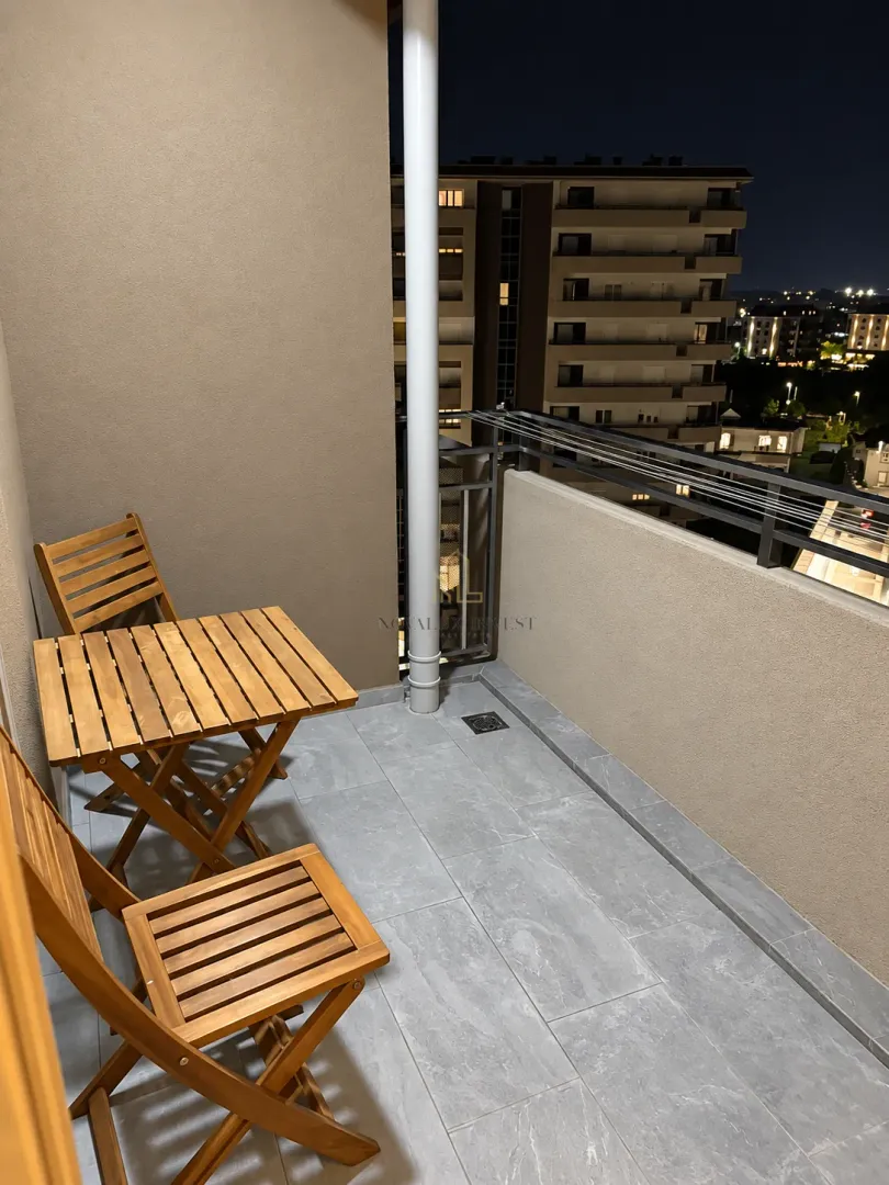 Small furnished balcony with a wooden table and chairs at night.