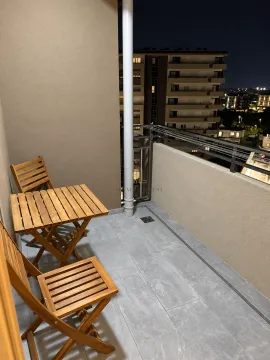 Small furnished balcony with a wooden table and chairs at night. - image 4